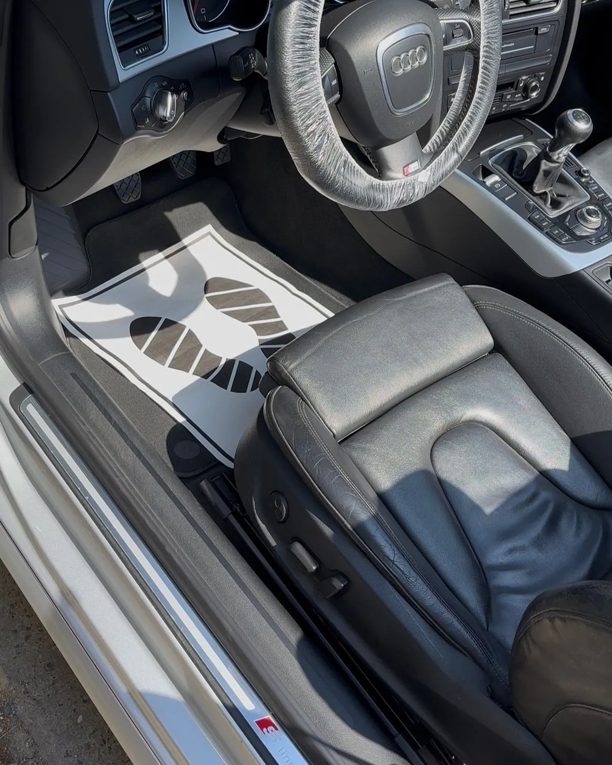 Poste de conduite d'une Audi A5 en cours de nettoyage, volant sous film et tapis de protection au sol